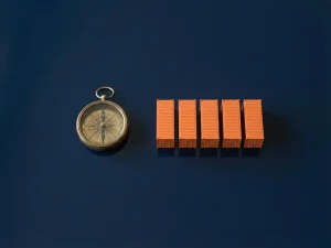 Messing kompas naast gestapelde oranje miniatuur zeecontainers op diepblauw oppervlak, minimalistisch bovenaanzicht