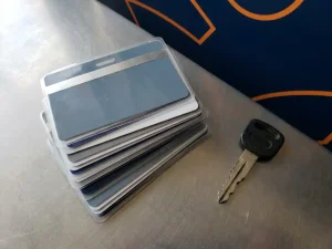 Gestapelde professionele certificeringskaarten en gelamineerde diploma's op gepolijst stalen oppervlak, heftrucksleutel ernaast, marineblauw met oranje accenten.