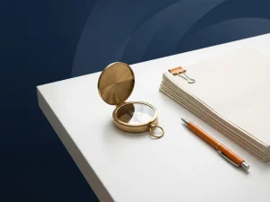 Messing kompas op wit bureau naast gestapelde documenten en oranje pen, minimalistisch plat gelegd met marineblauw accent.