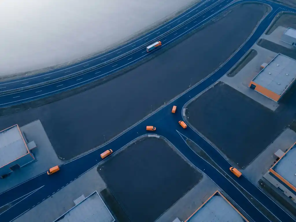Vrachtauto op snelweg met bestelwagens die afbuigen naar magazijnen, luchtfoto in marineblauw en oranje tinten.