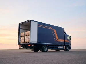 Vrachtwagentrailer met open deuren toont georganiseerde pallets, marineblauw met oranje accenten tegen ochtendhemel.